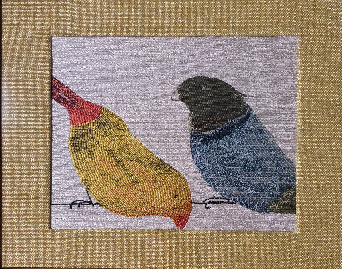 Close-up of yellow and blue woven birds surrounded by the textured gold-toned fabric mat.