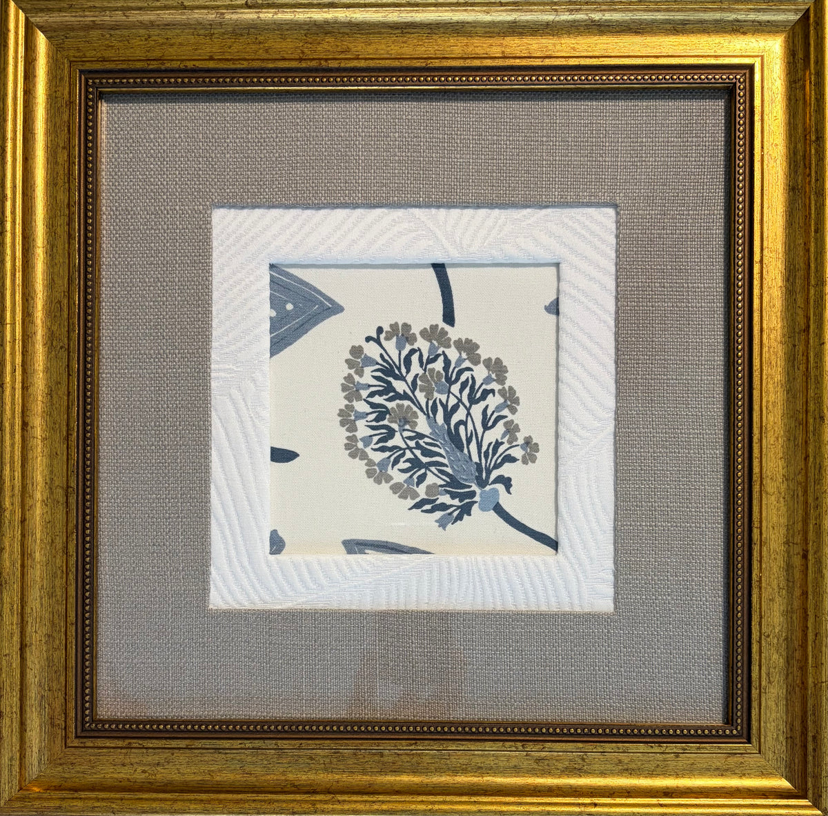 A framed square art print featuring a blue and gray botanical floral design on a cream background, surrounded by layered white textured mats and a wide gold-toned wooden frame.