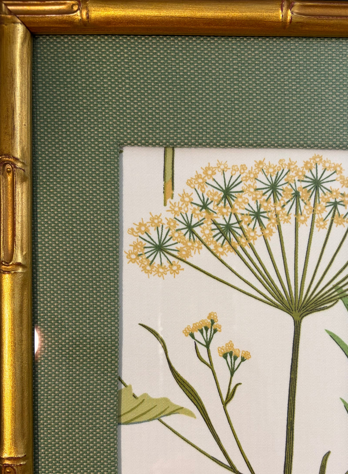 Upper-left detail of yellow flower clusters with the textured green mat and gold bamboo-style frame.