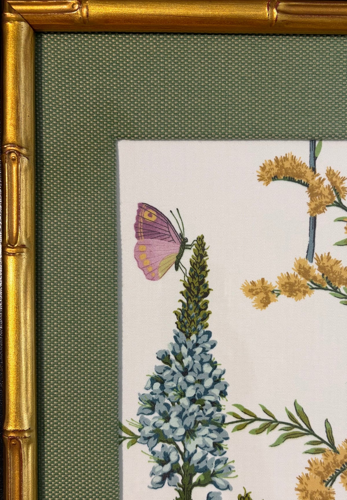 Upper-left detail showing a purple butterfly, blue flowers, green fabric mat and gold bamboo-style frame.